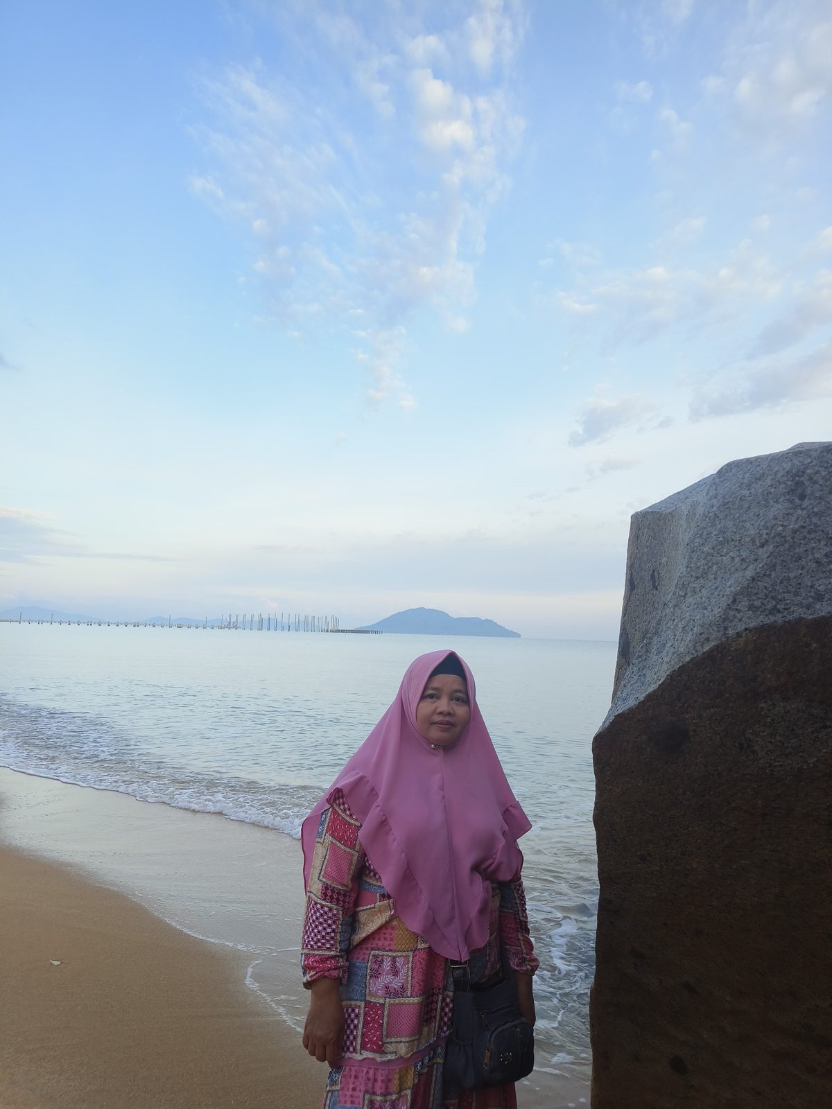 Ummi berjilbab pink di tepi pantai, laut dan pulau di kejauhan