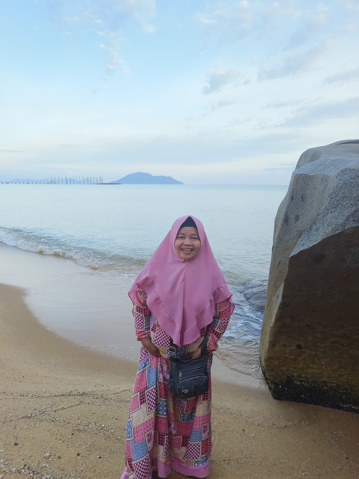Ummi berjilbab pink berdiri di tepi pantai berbatu