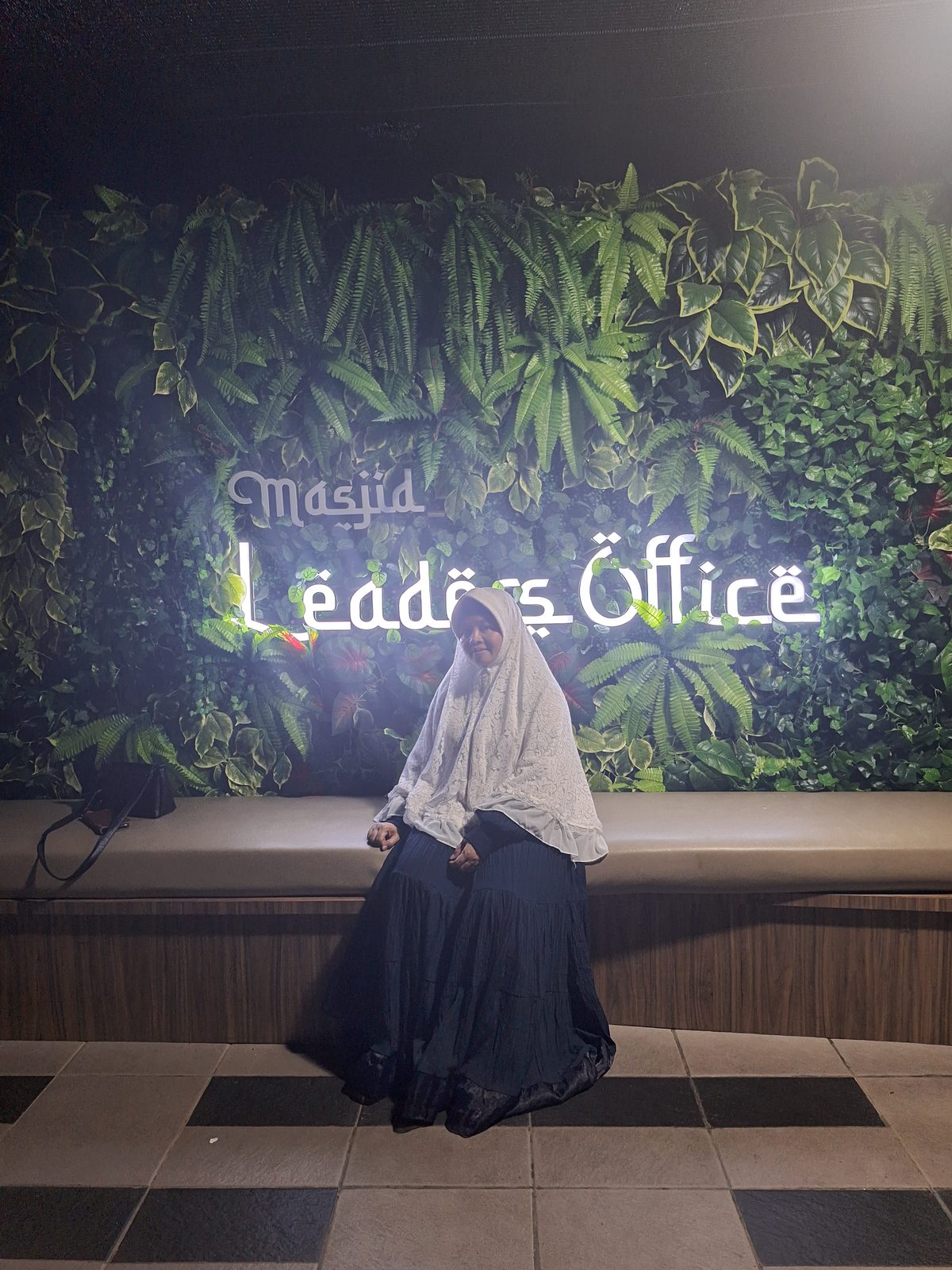 Ummi duduk di depan dinding tanaman bertuliskan Masjid Leaders Office
